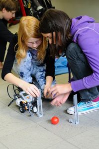 Foto von 2 Kindern die einen Legoroboter bedienen.